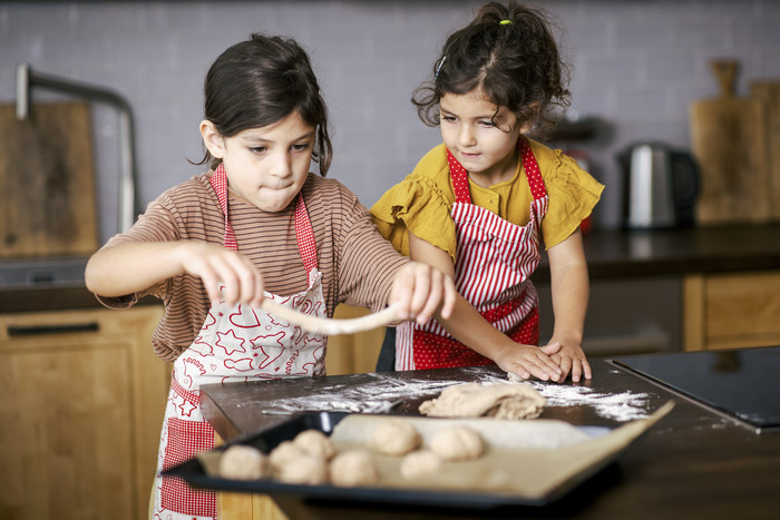 Zwei Kinder legen Teig in verschiedenen Formen auf ein Backblech