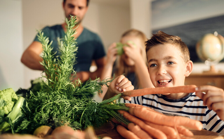 Familie kocht mit Kindern. Junge beißt in Möhre. 