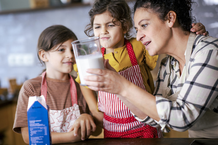 Eine Frau zeigt zwei Kindern ein Glas Milch