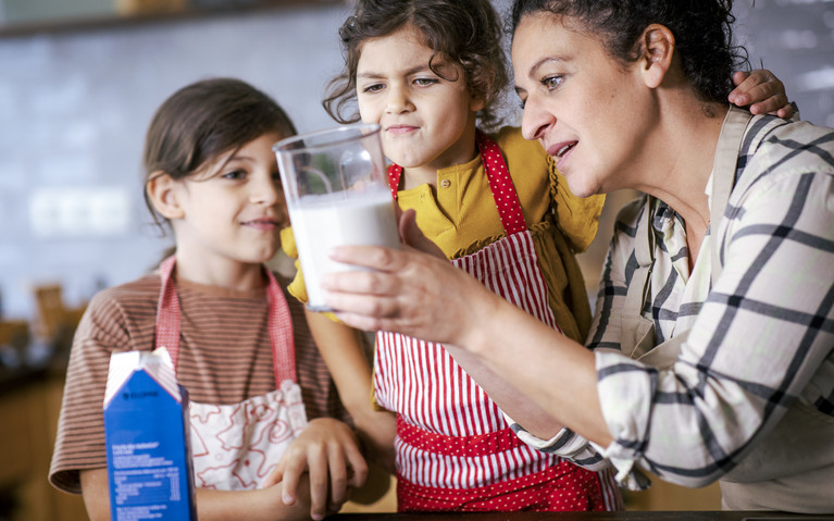 Eine Frau und zwei Kinder schauen sich Milch in einem Messbecher an