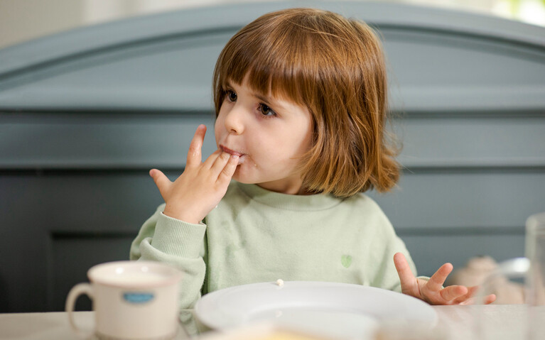 Kind lernt essen und leckt sich die Finger beim gemeinsamen Frühstück ab. 