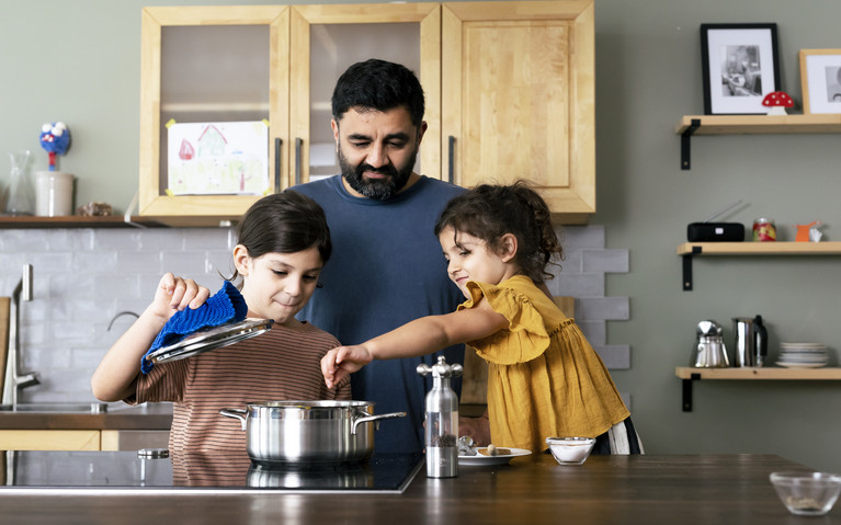 Ein Mann und zwei Kinder kochen zusammen am Herd