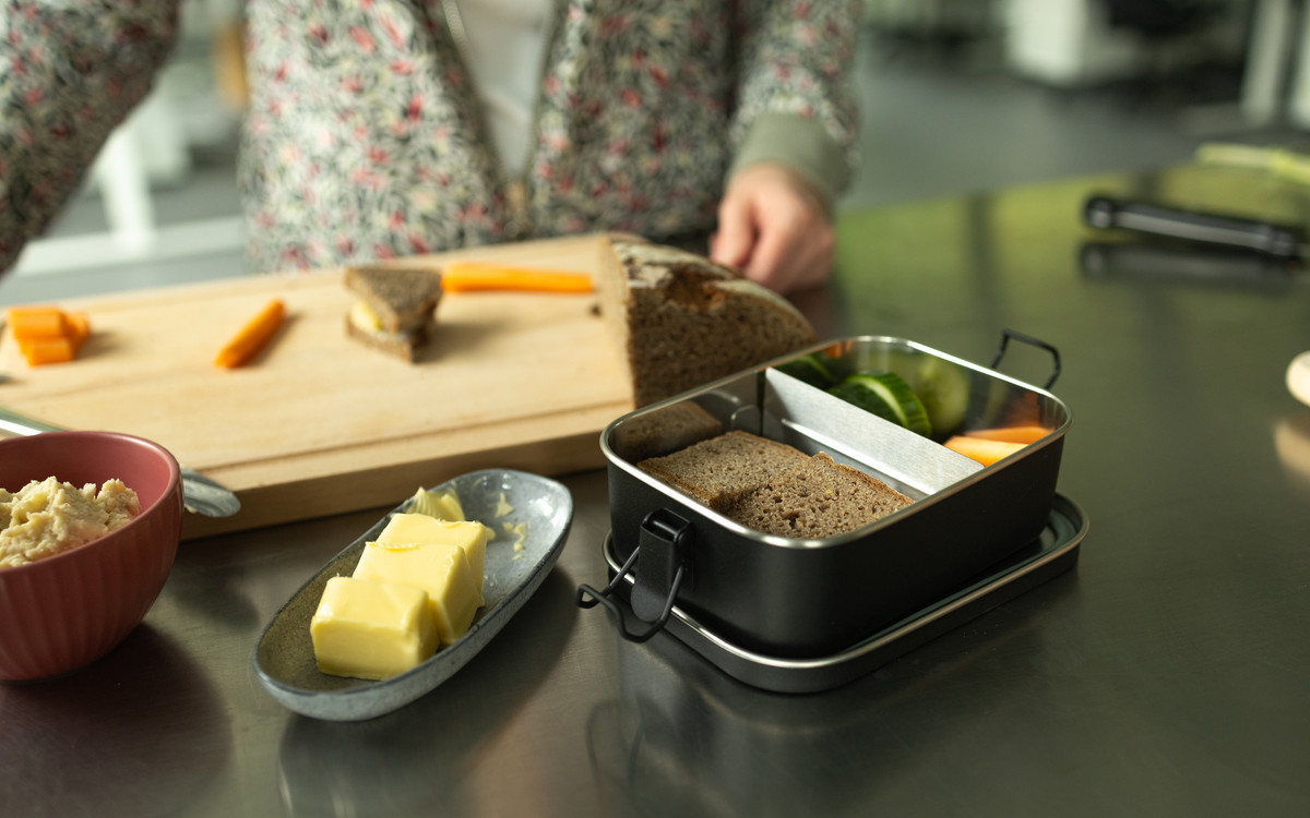 Eine Brotdose mit Brot, Obst und Gemüse, daneben ein Schälchen mit Butter
