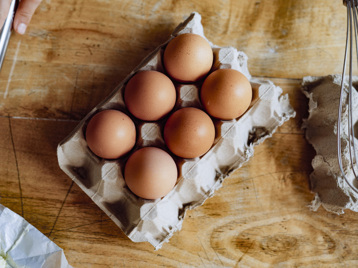 Sechs braune Eier in einem Eierkarton auf einem Holztisch