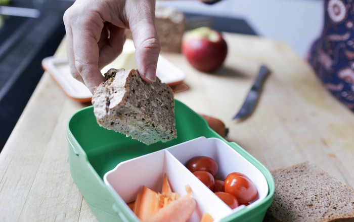 Eine Hand legt ein Brot in eine Brotdose