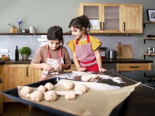 Zwei Kinder legen Teig auf ein Backblech