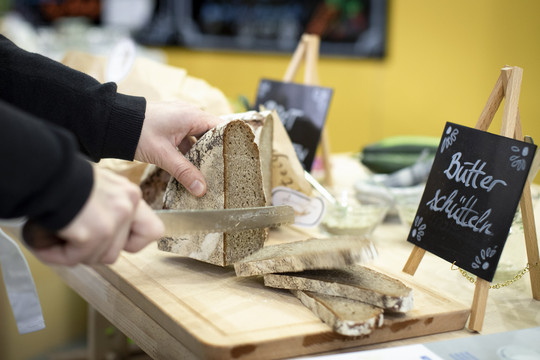 Brot wird aufgeschnitten, daneben ein Schild mit der Aufschrift "Butter schütteln"