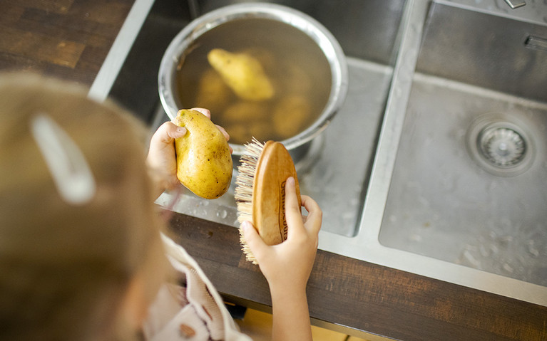 Kind bürstet Kartoffeln in der Spüle sauber.