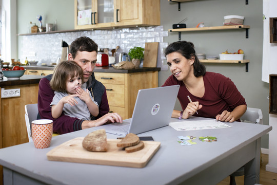 Zwei Erwachsene und ein Kind gucken auf einen Laptop