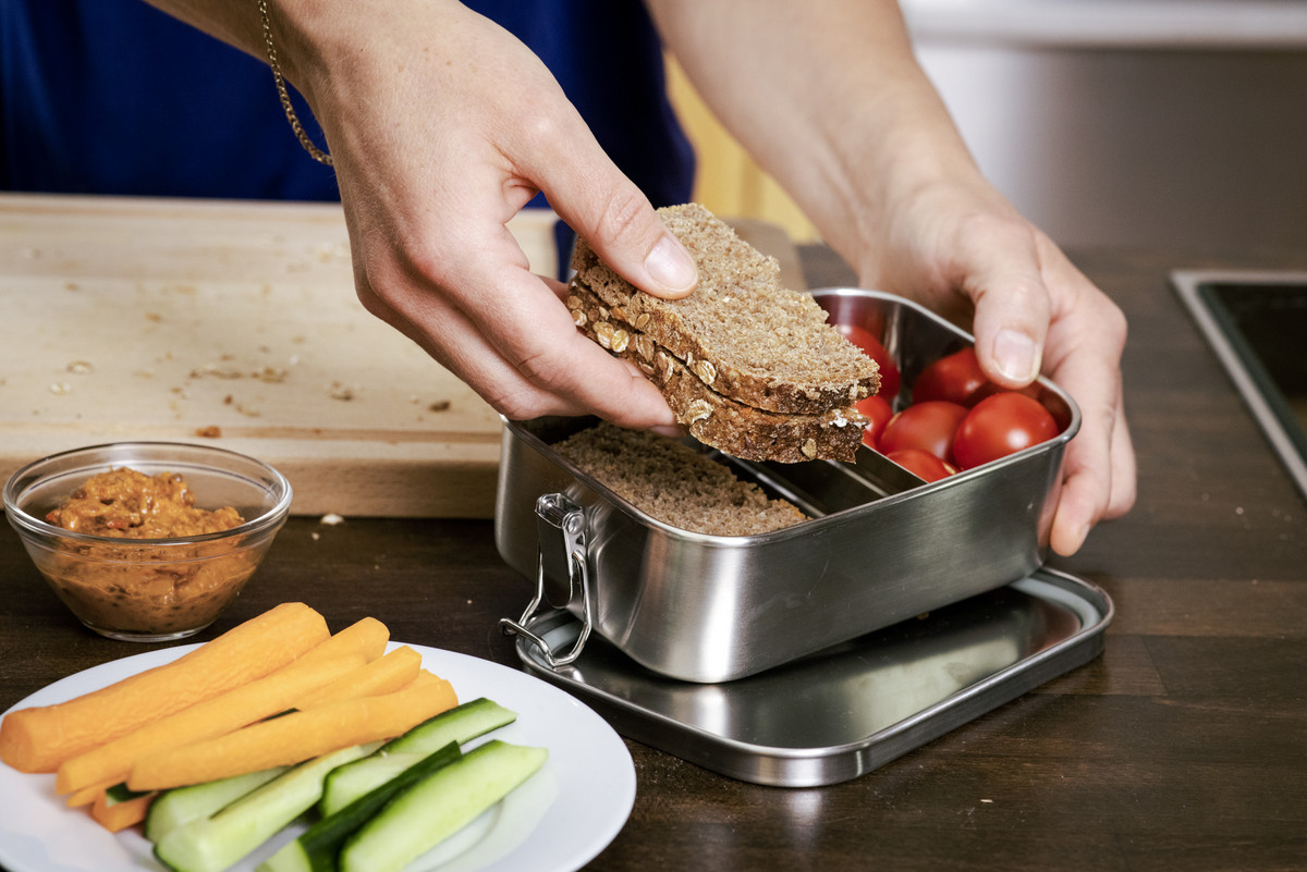 Eine Hand legt Brot zu Tomaten in eine Britdose